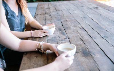 Kaksi naista istuvat pöydän äärellä ja juovat kahvia.